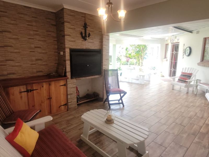 A spacious covered patio featuring tiled flooring, a built-in braai area with stone cladding, and built-in cabinetry, ideal for outdoor entertaining.