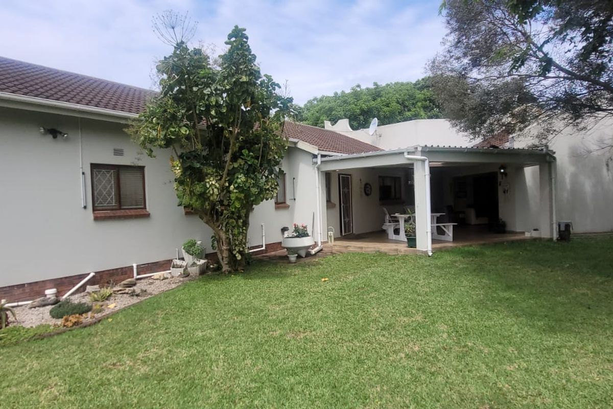 Rear view of the house featuring a covered patio area, tiled roof, and a well-maintained lawn garden.