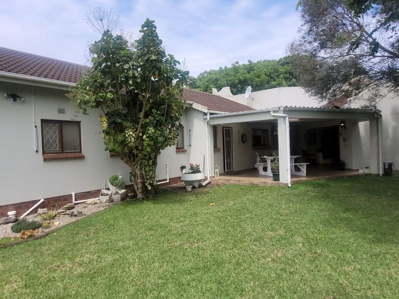 Rear view of the house featuring a covered patio area, tiled roof, and a well-maintained lawn garden.