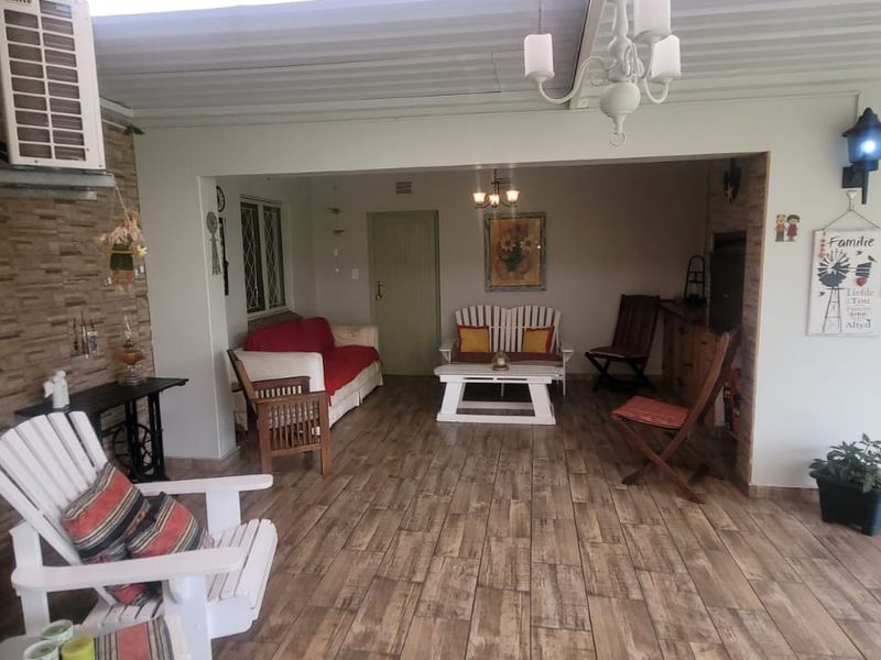A spacious covered patio featuring wood-look tiled flooring, a built-in braai area, and direct access to the garden, ideal for outdoor entertaining.