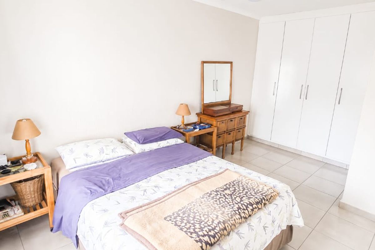 A well-lit bedroom featuring neutral tiled flooring, built-in white cabinetry, and coved ceiling details, offering a clean and functional living space.