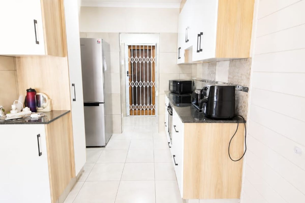 A functional kitchen featuring modern white and wood-tone cabinetry, granite countertops, tiled flooring, and a secure rear exit door.