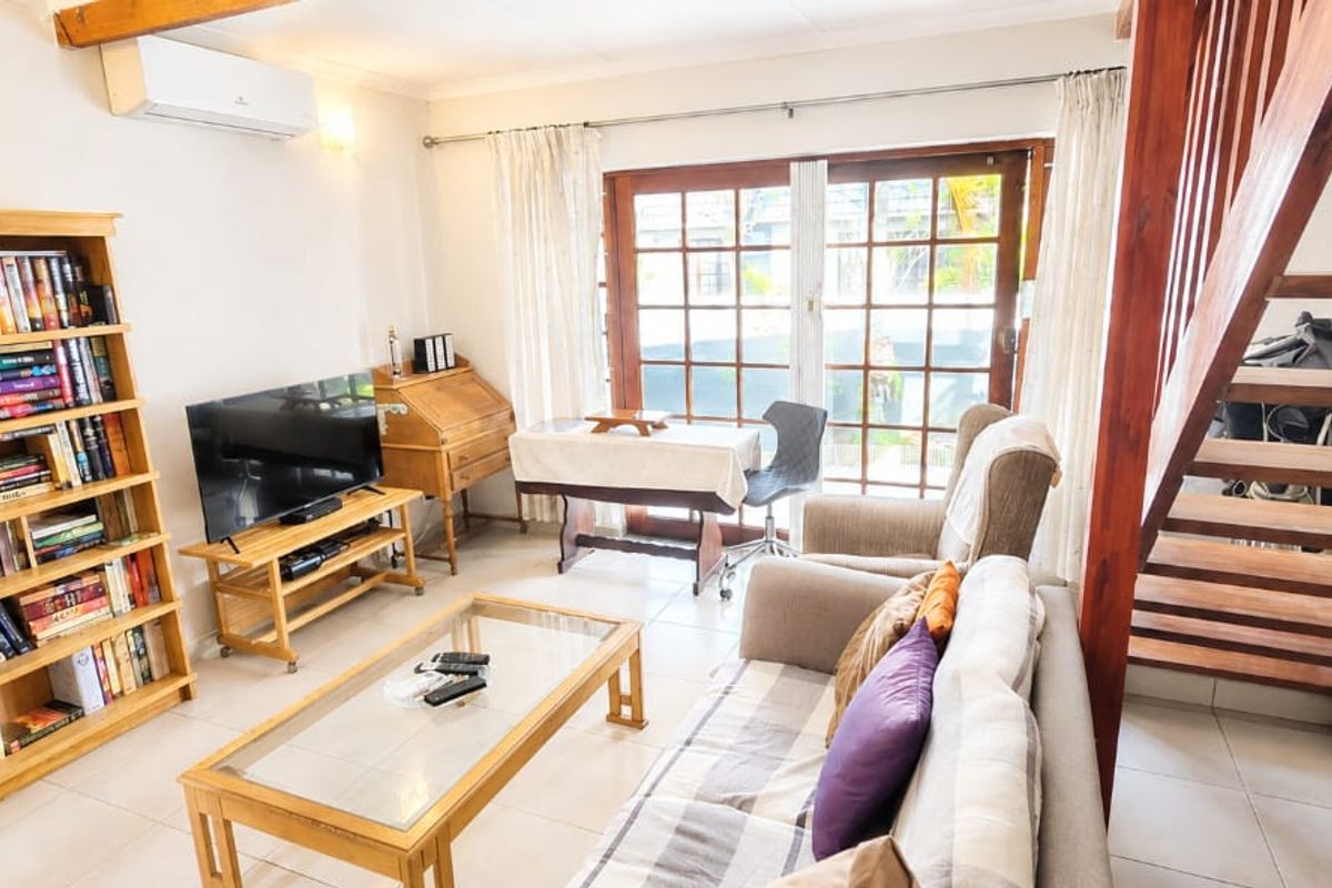 A cozy living room featuring tiled floors, a wooden staircase, and french doors leading to the exterior, equipped with a wall-mounted air conditioning unit.
