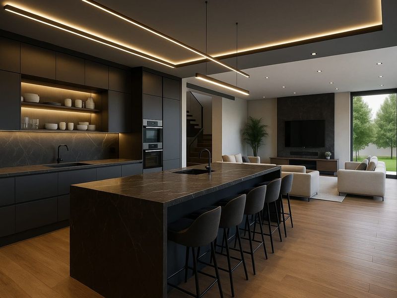 Modern open-plan living area featuring a sleek dark kitchen with stone island, integrated appliances, and seamless flow to the lounge with recessed lighting.