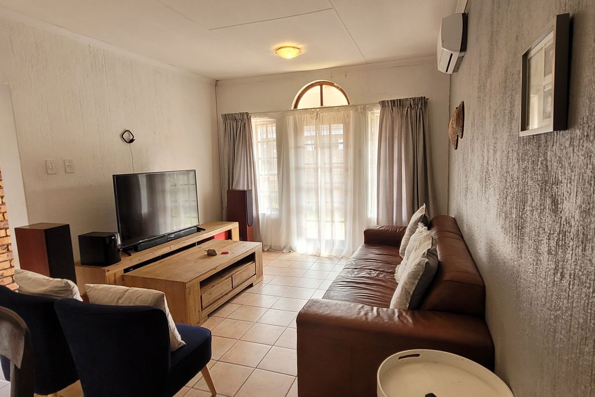 A comfortable living room featuring tiled flooring, a textured wall finish, and an arched window providing natural light, equipped with a wall-mounted air conditioner.