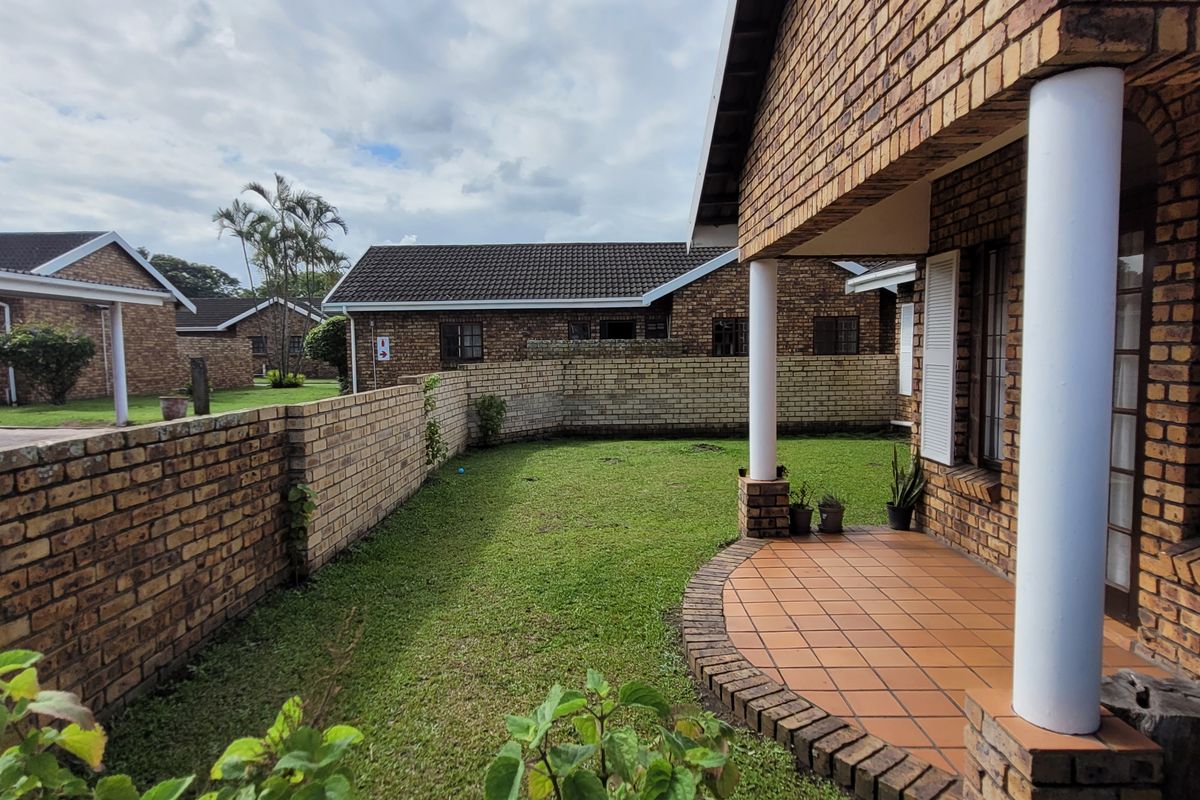 A rear view of the townhouse featuring a face-brick facade, a covered tiled patio, and a private grassed garden area enclosed by brick walls.