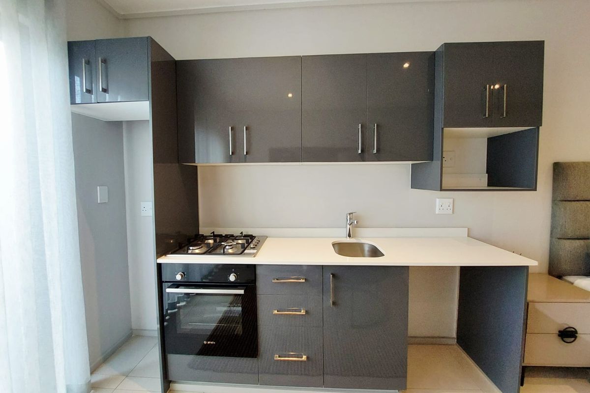 Compact modern kitchenette featuring high-gloss grey cabinetry, integrated gas hob, built-in oven, and a sleek white countertop with a stainless steel sink.