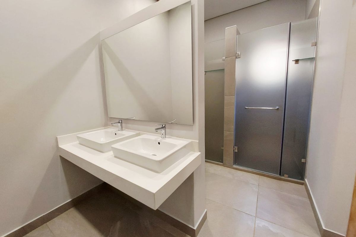 Modern bathroom featuring a double vanity with vessel sinks, a large wall-mounted mirror, and a glass-enclosed walk-in shower with neutral floor tiling.