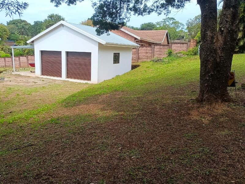 A view of the rear yard featuring a detached double garage with roller shutter doors and a brick boundary wall.