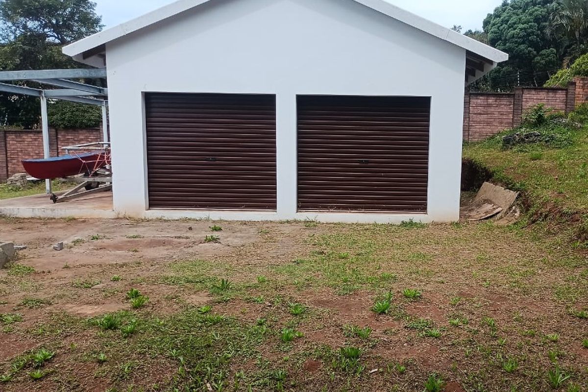 A detached double garage with roller doors situated on a residential plot with surrounding brick boundary walls.