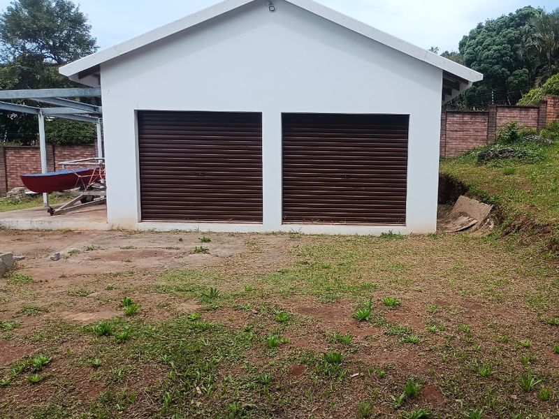 A detached double garage with roller doors situated on a residential plot with surrounding brick boundary walls.