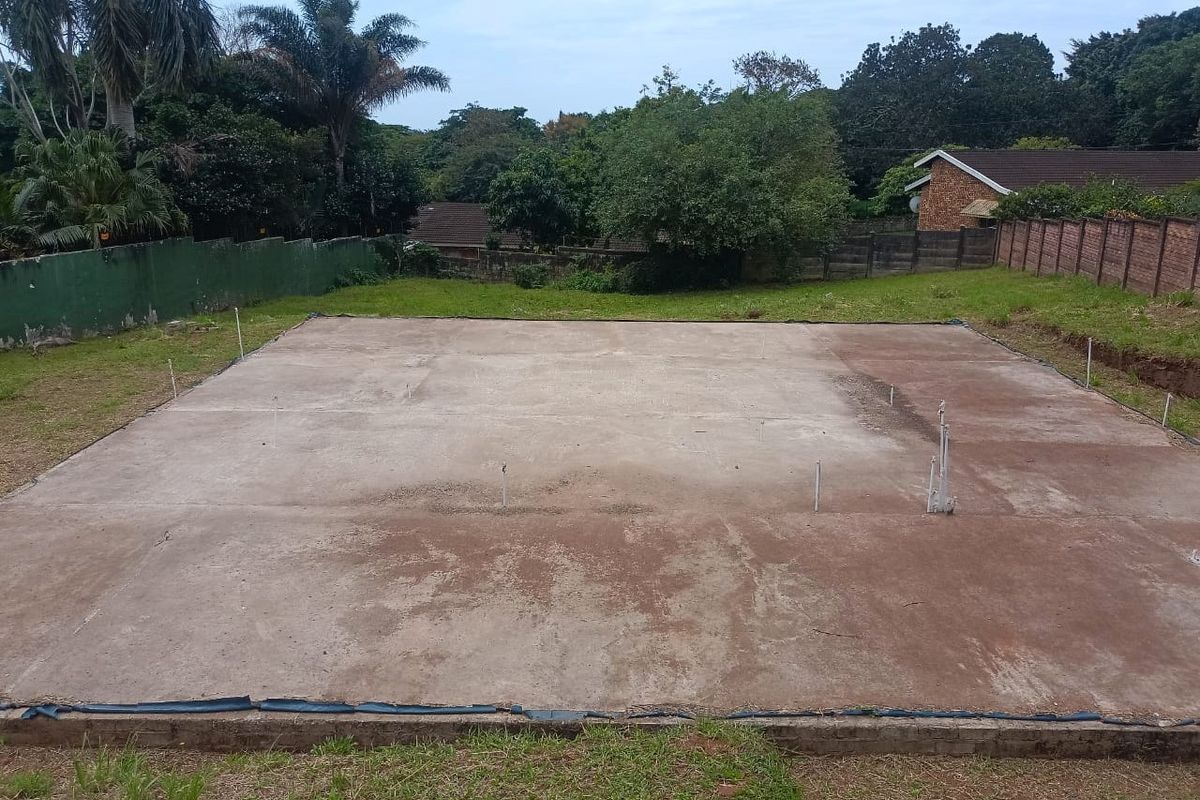 A vacant residential plot featuring a prepared concrete slab foundation with visible plumbing rough-ins, ready for new construction.