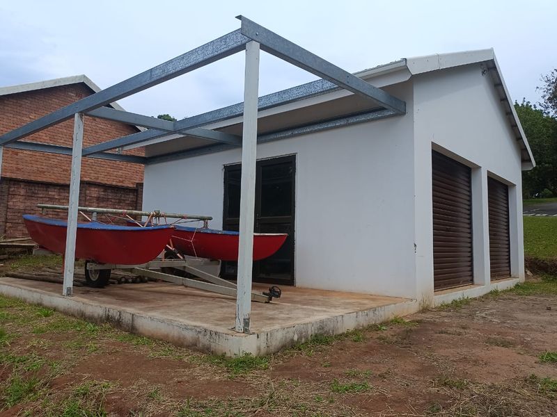 A detached garage structure featuring two roller shutter doors, a side glass sliding door, and an attached steel-framed pergola over a concrete slab.