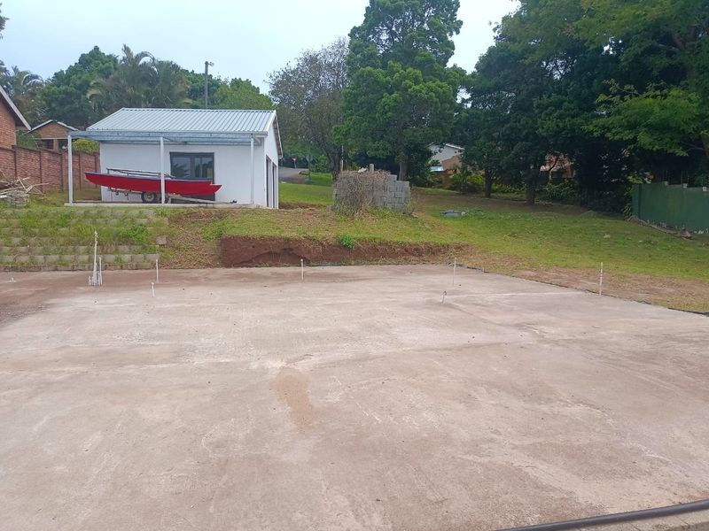 A vacant residential plot featuring a concrete slab foundation, retaining wall, and a detached garage structure in the background.