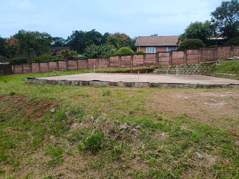 A vacant residential plot featuring a prepared concrete slab foundation, retaining walls, and brick perimeter fencing, ready for further development.