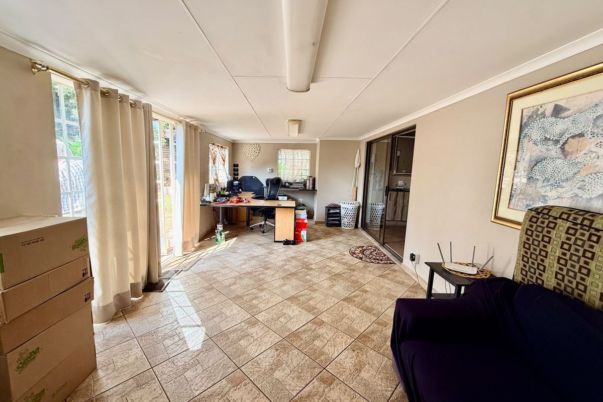 A spacious living area featuring tiled flooring, sliding glass doors providing natural light, and a built-in desk area, suitable for a home office or lounge.