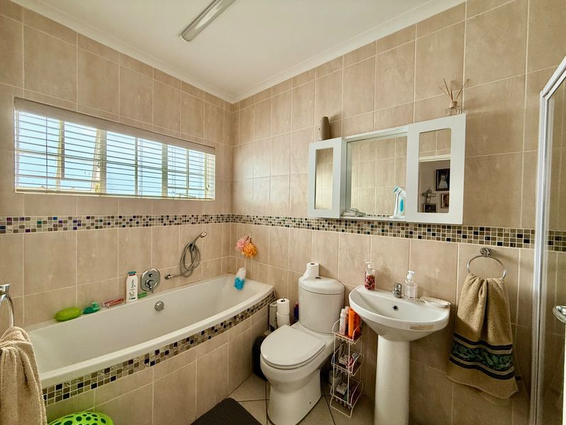 A functional bathroom featuring a bathtub, pedestal basin, toilet, and neutral wall tiling with a decorative mosaic border.