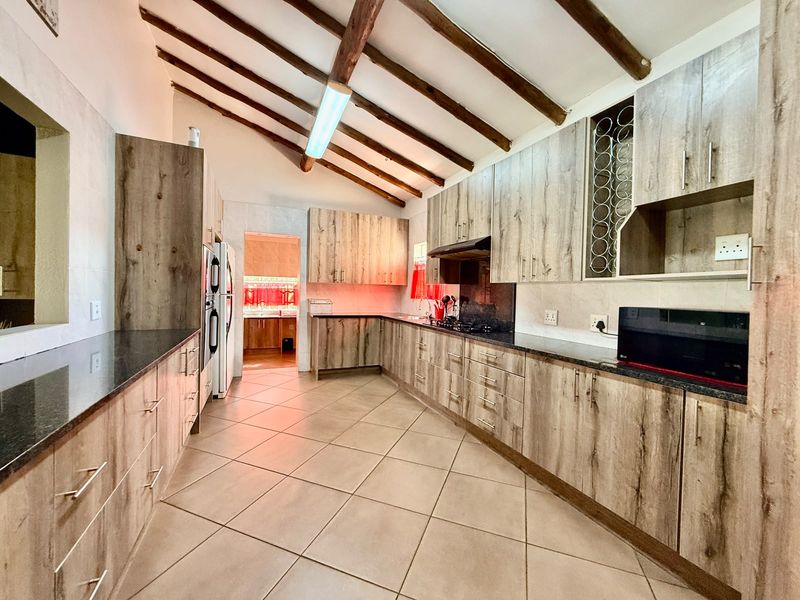 Spacious kitchen featuring exposed timber ceiling beams, modern laminate cabinetry, granite countertops, and integrated appliances with tiled flooring.