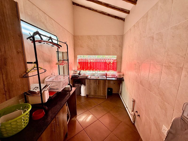 A functional laundry room featuring tiled walls and floors, built-in cabinetry with a double basin sink, and exposed timber ceiling beams.