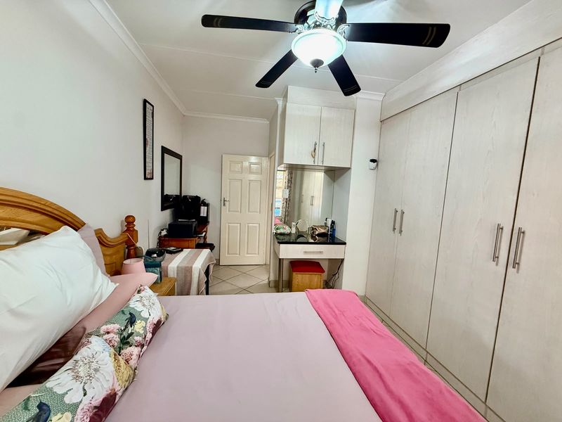A well-maintained bedroom featuring extensive built-in cupboards, a dedicated vanity area with overhead storage, and a central ceiling fan.