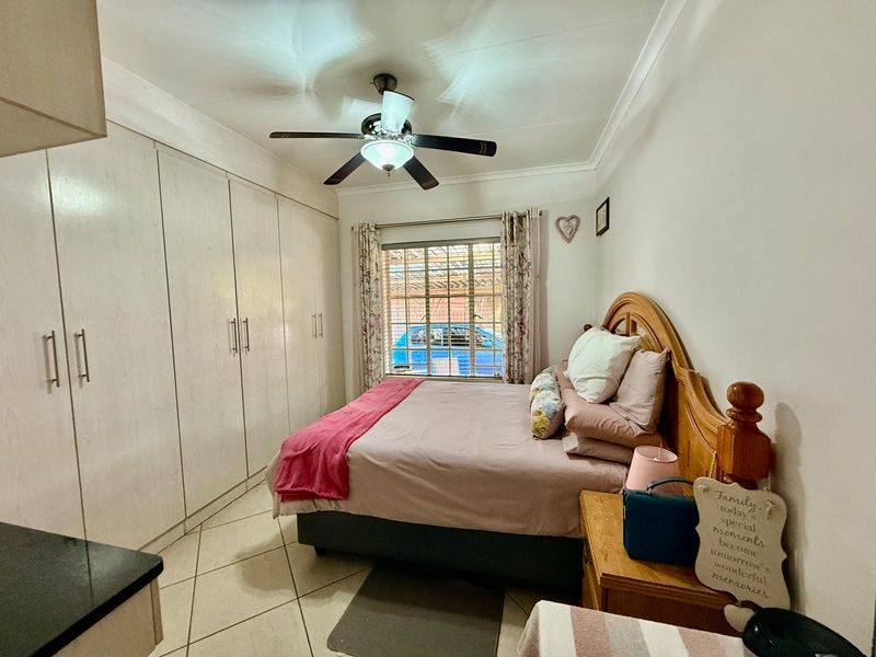 A bedroom featuring built-in cupboards, tiled flooring, and a ceiling fan, with security bars on the window.