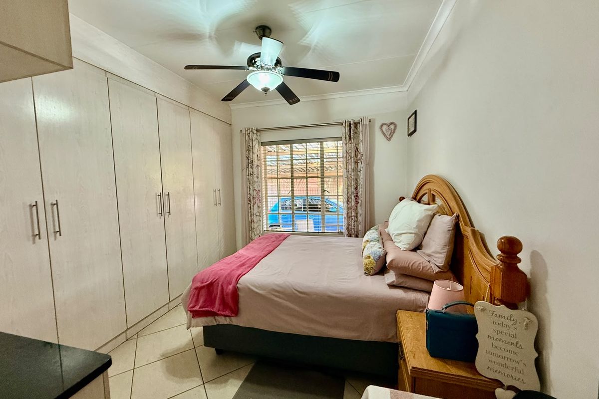 A bedroom featuring built-in cupboards, tiled flooring, and a ceiling fan, with security bars on the window.