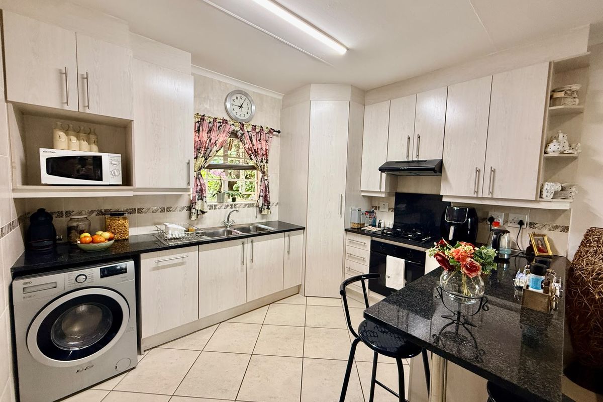 A functional kitchen featuring light wood-grain cabinetry, dark granite countertops, a built-in oven with gas hob, and an integrated washing machine.