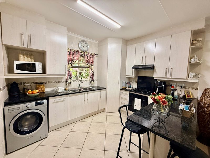 A functional kitchen featuring light wood-grain cabinetry, dark granite countertops, a built-in oven with gas hob, and an integrated washing machine.