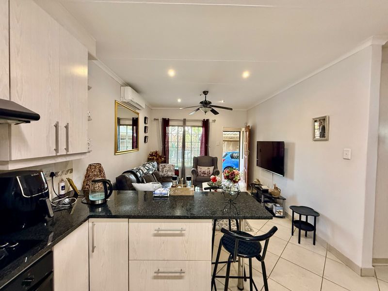 Open-plan living area featuring a modern kitchen with granite countertops, tiled flooring, and a split-system air conditioner, seamlessly flowing into the lounge space.