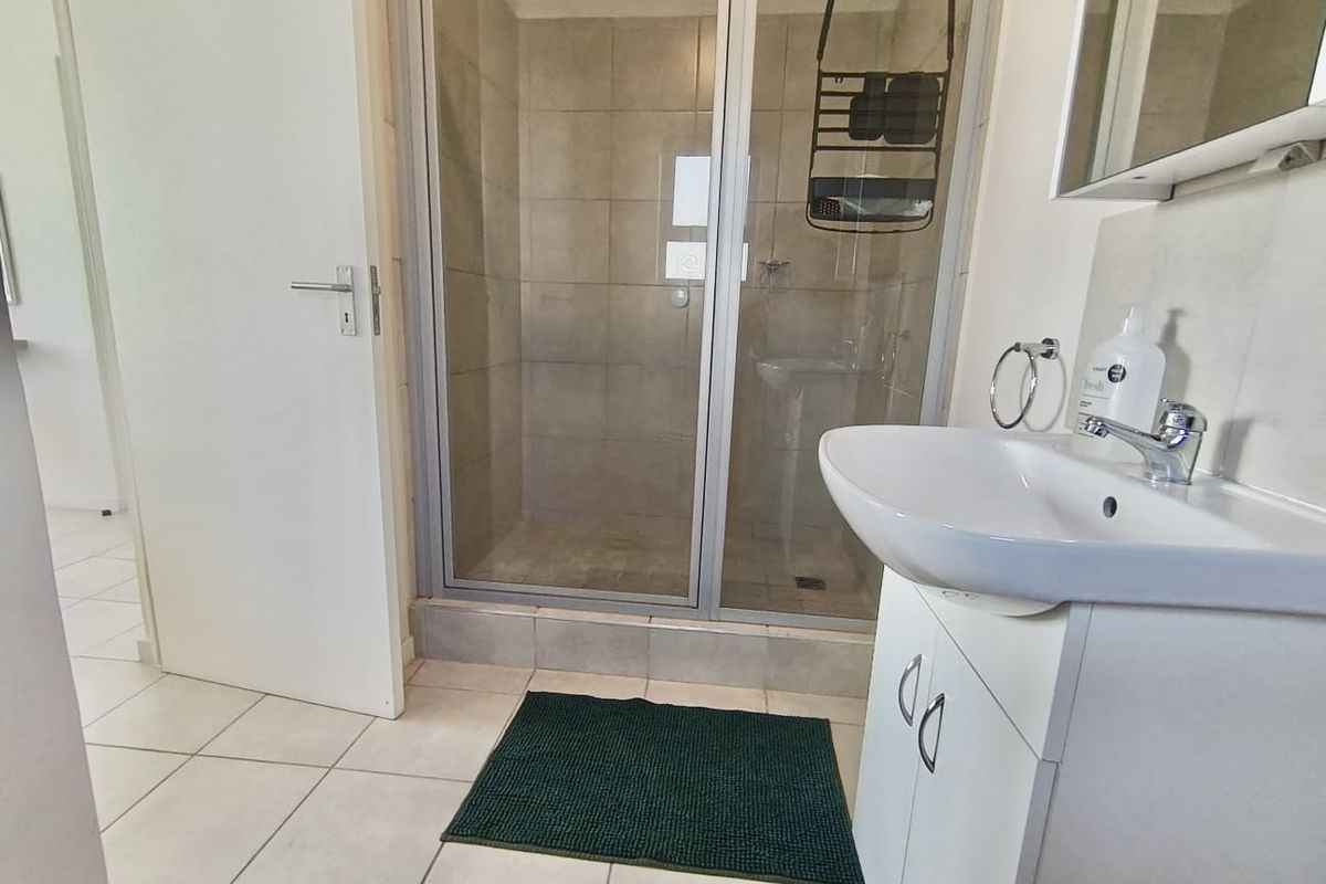 A functional bathroom featuring a tiled shower enclosure, a white vanity cabinet with a ceramic basin, and neutral floor tiling.