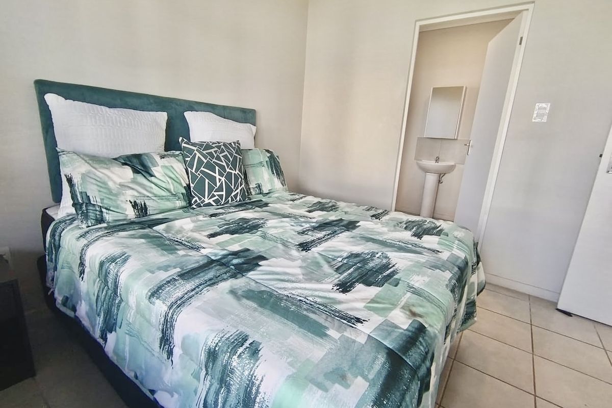 A bedroom featuring tiled flooring with an adjoining en-suite bathroom equipped with a pedestal basin and wall-mounted mirror.