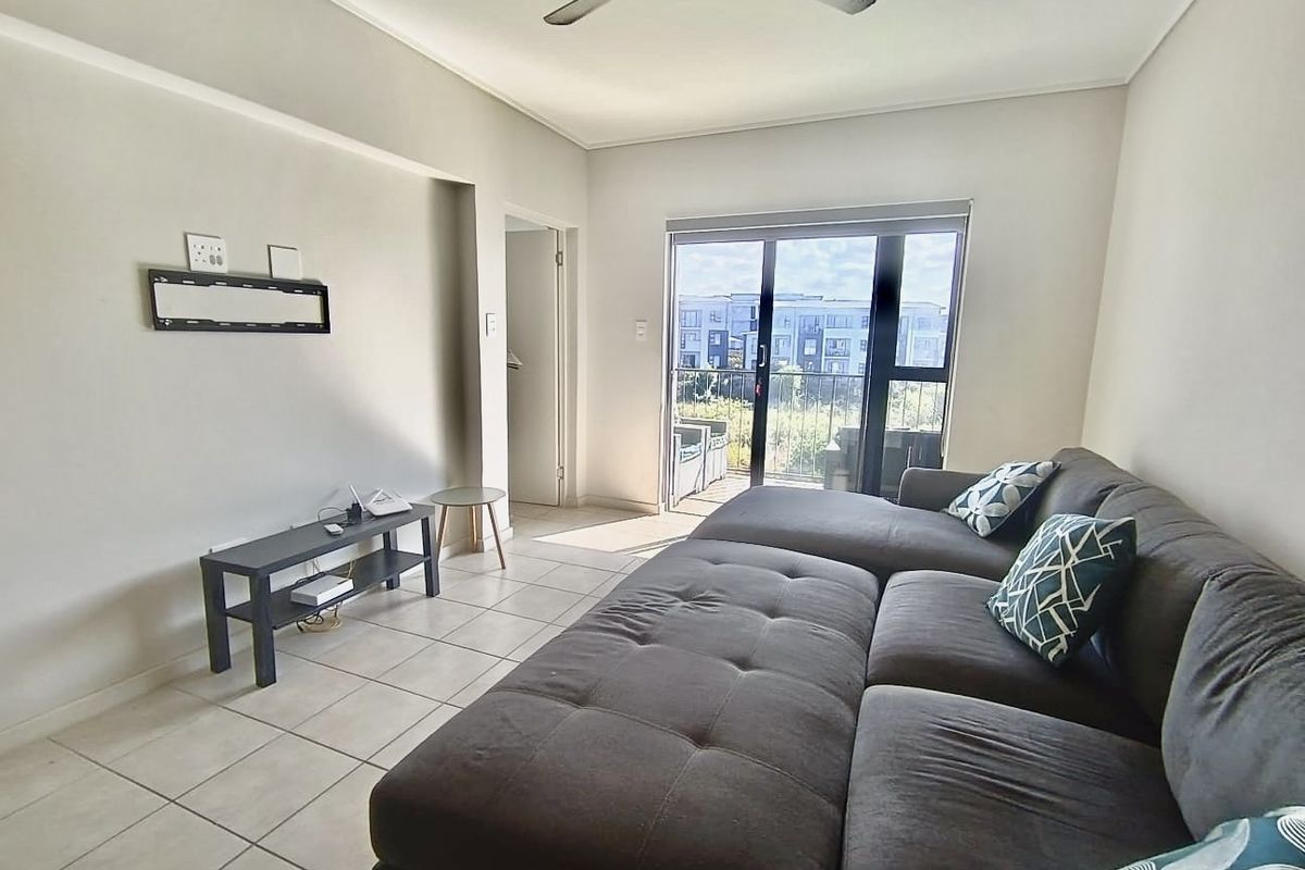 A bright living room featuring tiled flooring, a ceiling fan, and a sliding glass door that opens onto a balcony.