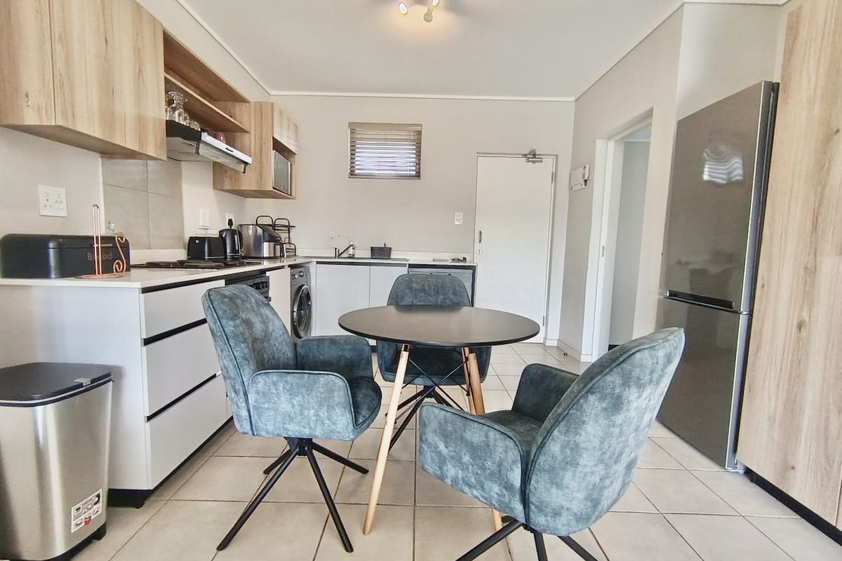 Modern open-plan kitchen and dining area featuring contemporary cabinetry, tiled flooring, and integrated appliances in a well-maintained apartment setting.