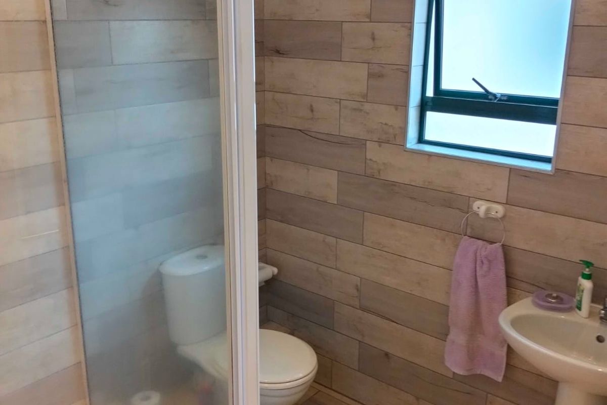 A modern bathroom featuring wood-look wall and floor tiles, a glass shower enclosure, a pedestal basin, and a toilet.