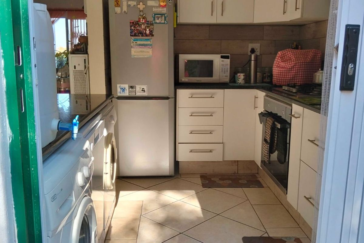 Compact kitchen featuring white cabinetry, tiled backsplash, built-in oven, extractor fan, and integrated laundry plumbing connections.