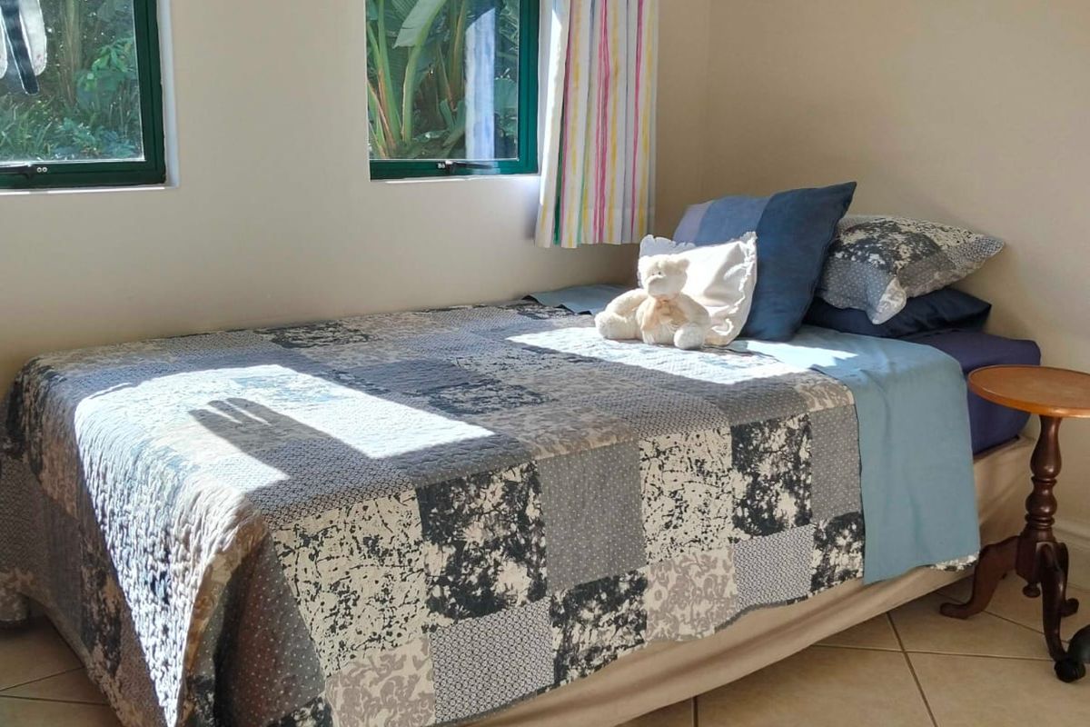 A functional bedroom featuring neutral tiled flooring and large windows with dark aluminium frames, providing natural light and garden views.
