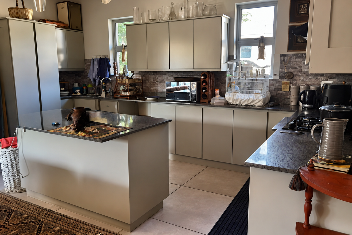 Modern kitchen featuring a central island, granite countertops, ample built-in cabinetry, and a gas hob, finished with neutral tones and tiled flooring.