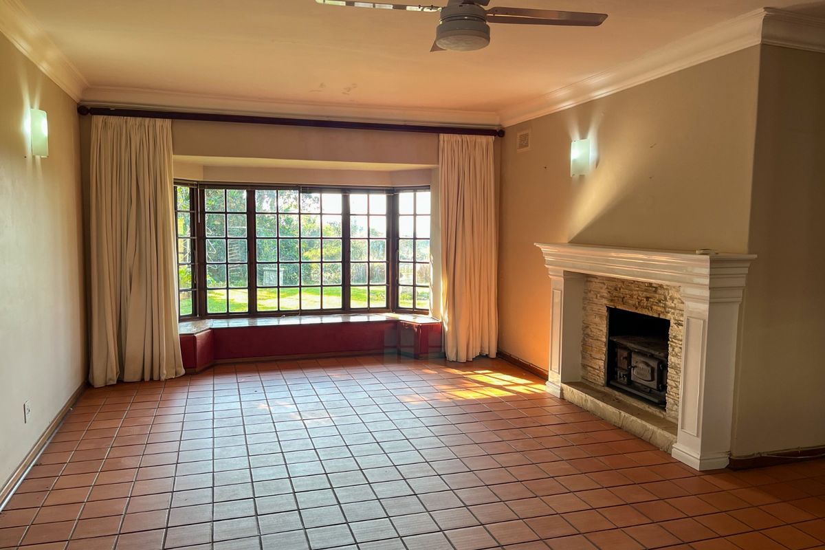 Spacious living room featuring a large bay window, a built-in fireplace with stone detailing, tiled flooring, and a ceiling fan.