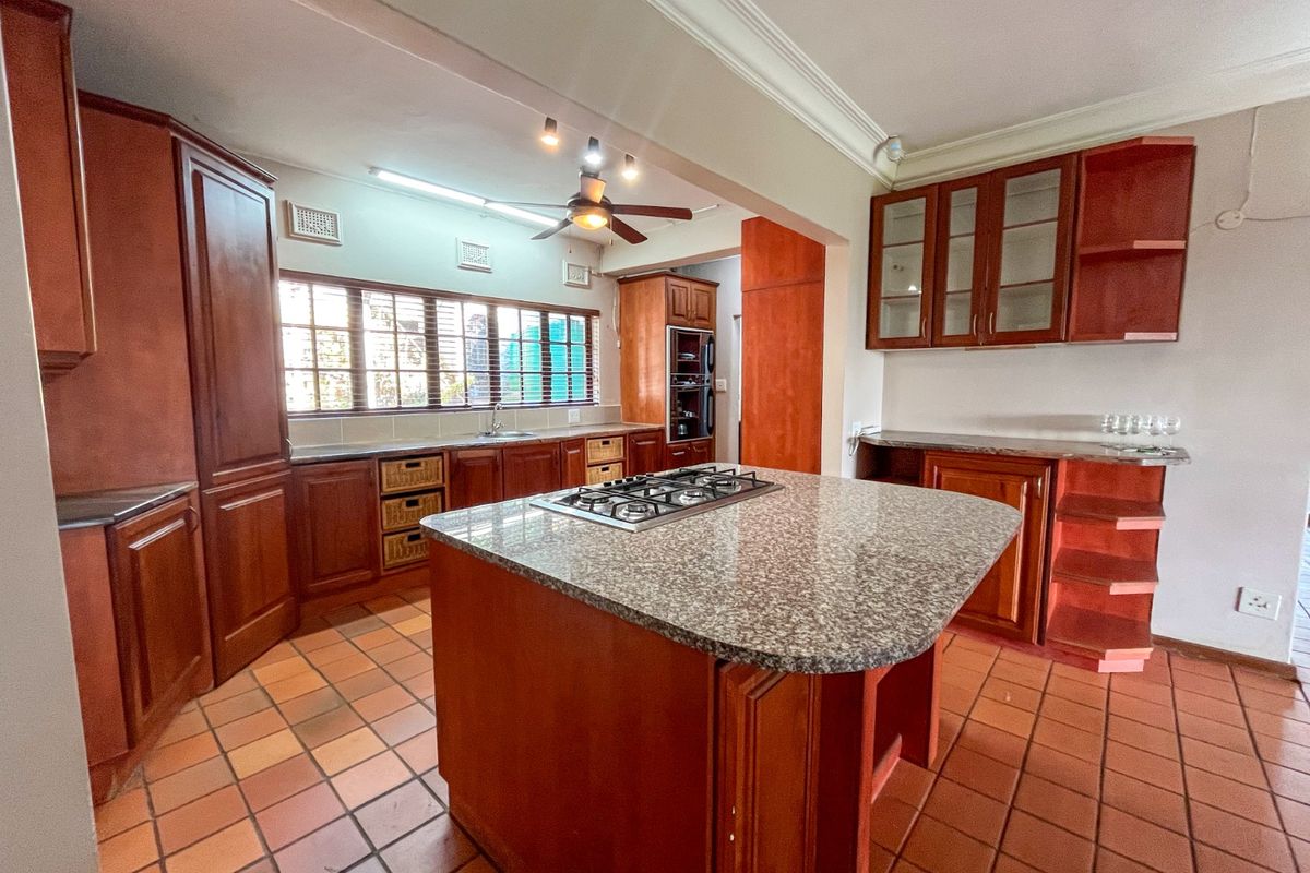 Spacious kitchen featuring wooden cabinetry, granite countertops, a central island with a gas hob, and tiled flooring.