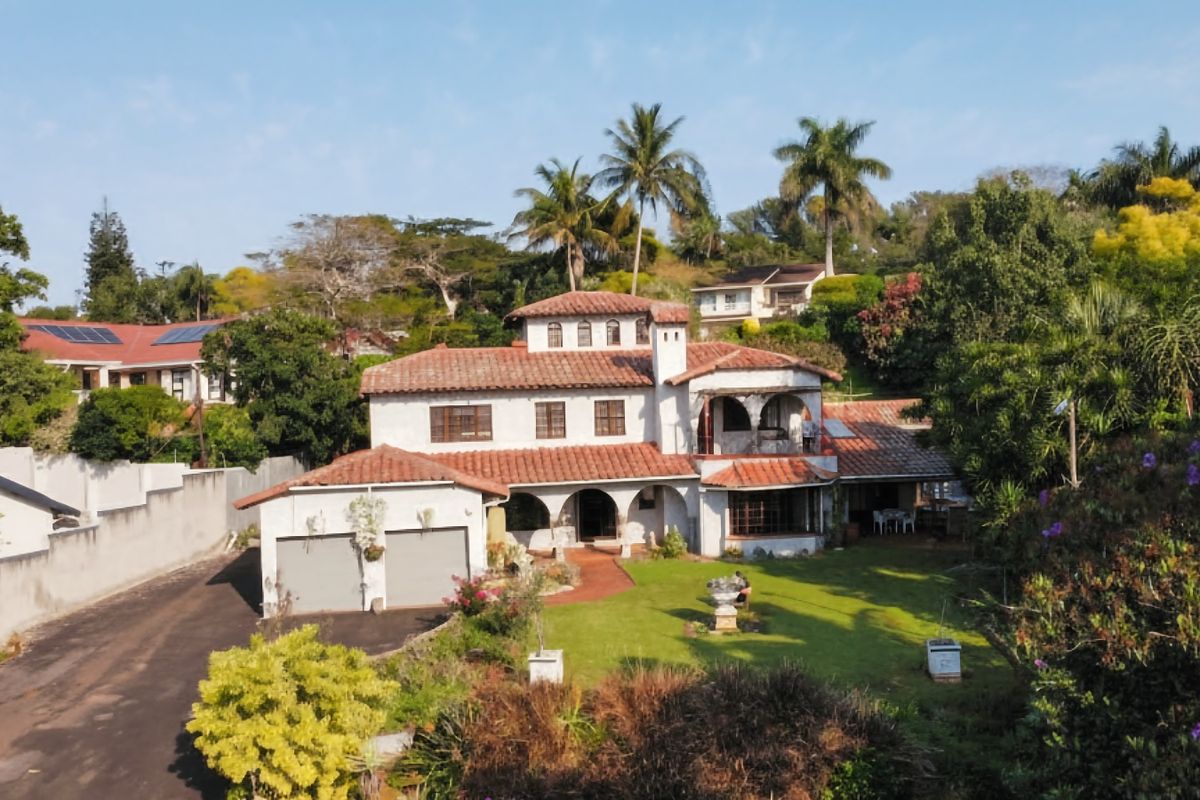 Aerial view of a Mediterranean-style two-story house featuring a terracotta tile roof, arched architectural details, and a spacious front garden with a paved driveway.