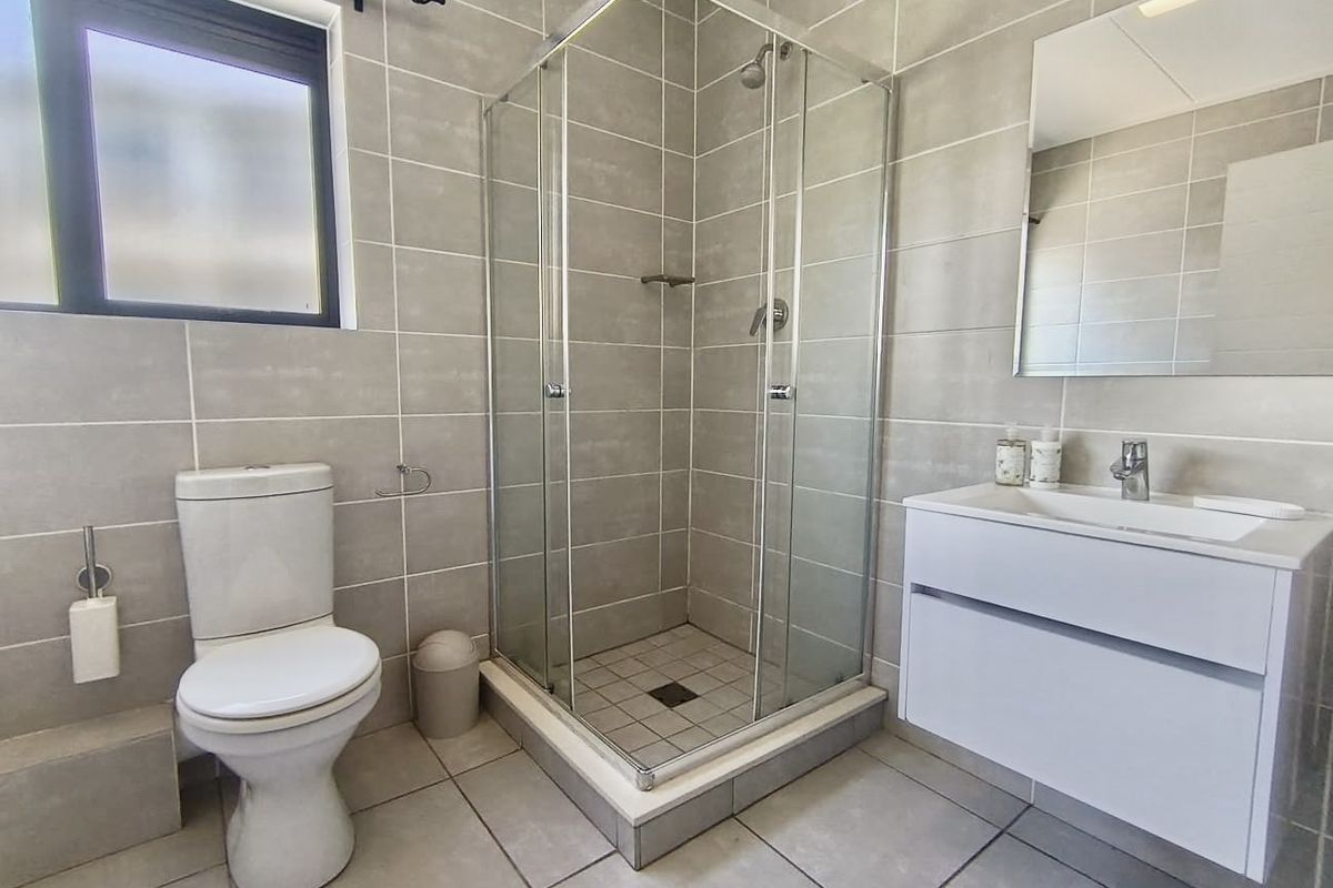Modern bathroom featuring a glass shower enclosure, white vanity cabinet with basin, wall mirror, and neutral floor-to-ceiling tiling.