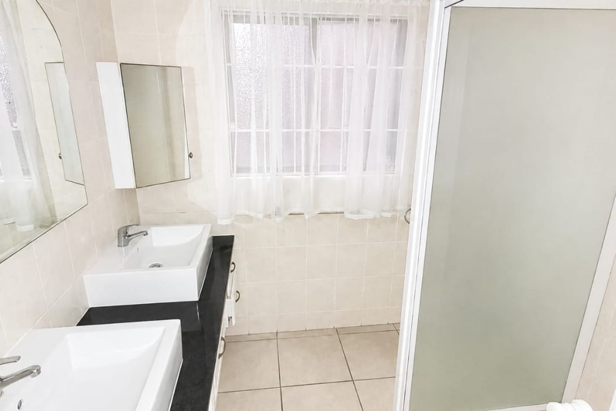 A clean, functional bathroom featuring a double vanity with a dark countertop, tiled walls, and a separate shower enclosure.