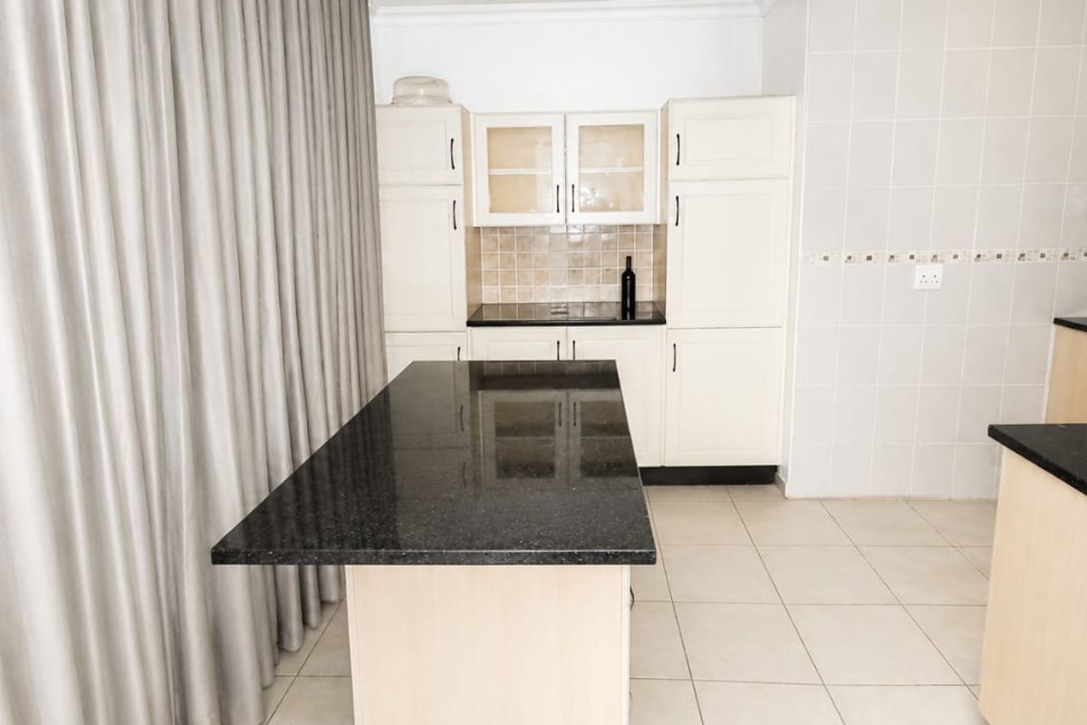 A functional kitchen featuring light-toned cabinetry, dark granite countertops, a central island, and neutral tiled flooring throughout.
