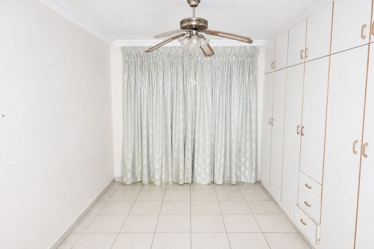 A spacious bedroom featuring neutral tiled flooring, a ceiling fan, and extensive built-in cupboard storage.