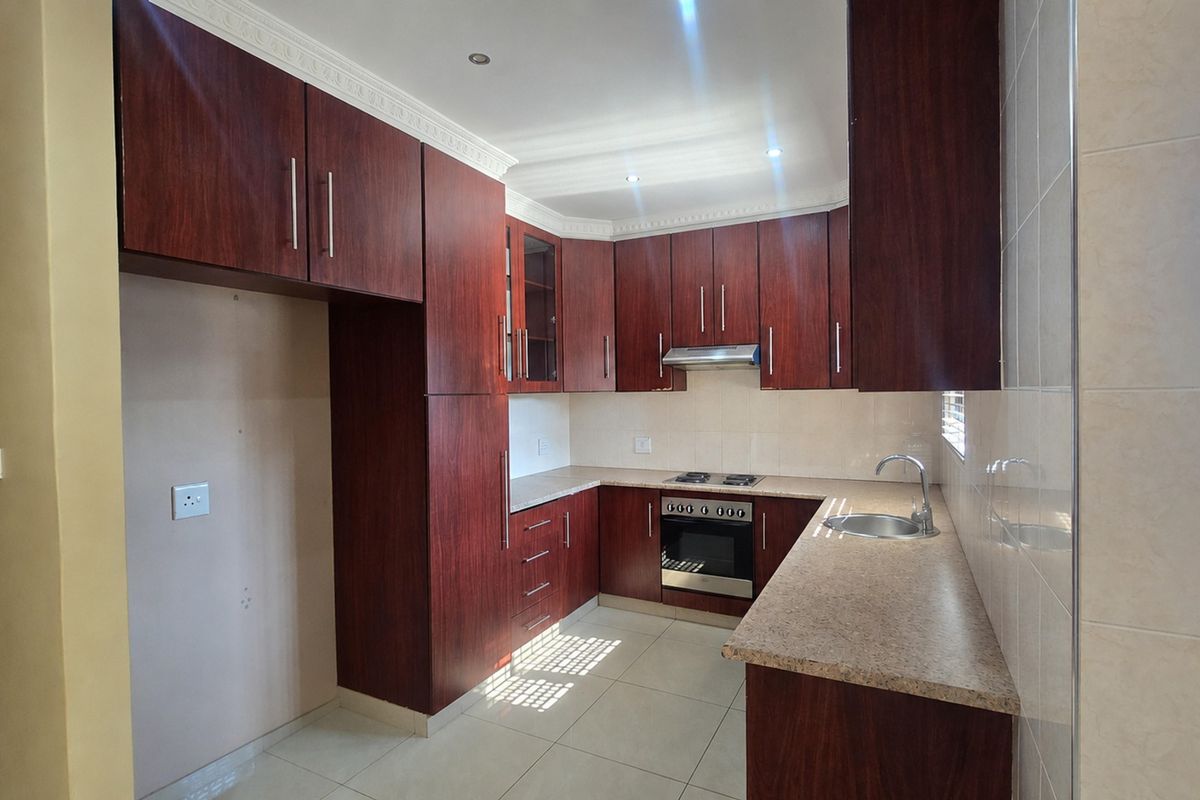 A clean, functional kitchen featuring dark wood cabinetry, stone-look laminate countertops, built-in oven and hob, and tiled flooring.