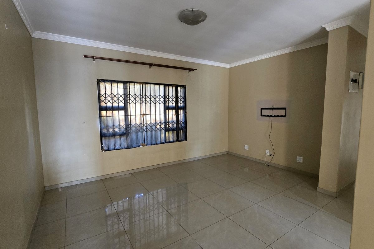 An empty living room featuring tiled flooring, neutral walls, and a window fitted with a security gate.