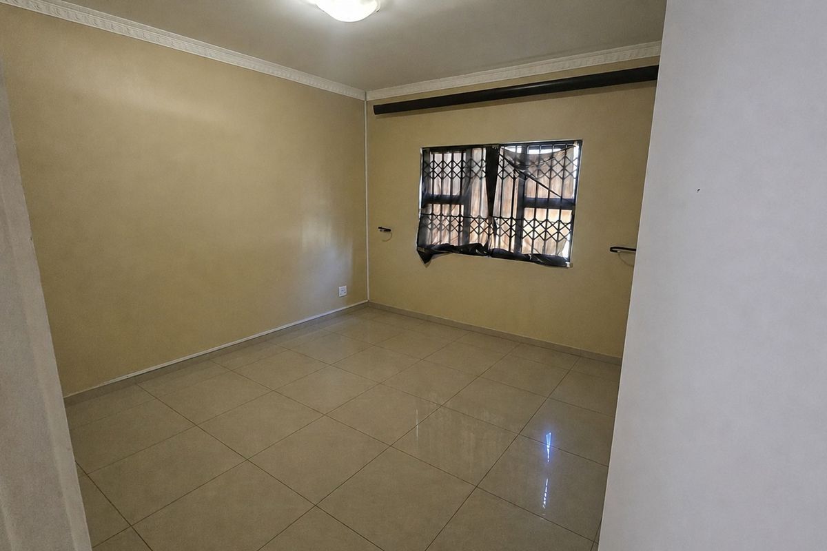 An empty bedroom featuring neutral tiled flooring, ceiling cornice detailing, and a window fitted with a security gate.