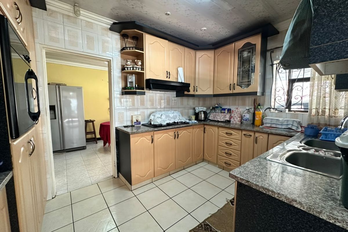 A functional kitchen featuring light wood cabinetry, granite countertops, tiled flooring, and a double bowl sink, with an adjacent view into the dining area.