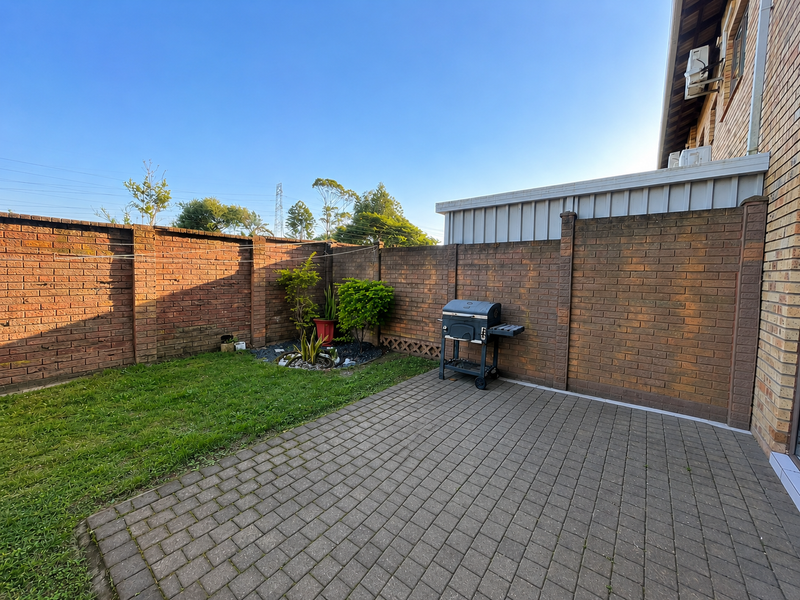 A private rear courtyard featuring a paved patio area, a small lawn, and high brick boundary walls for added privacy.