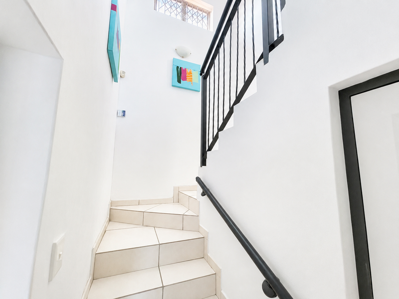 A bright, modern staircase featuring tiled steps, a sleek black metal balustrade, and a matching handrail, leading to an upper level.